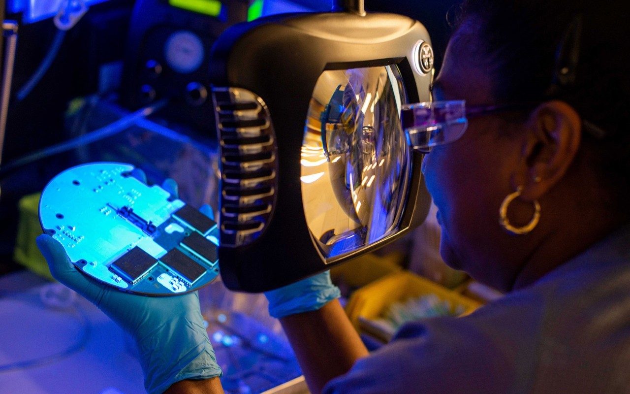 female inspector examining a motherboard under a magnifying glass 